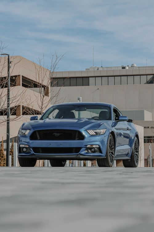 Free Blue Ford Mustang parked in a modern urban environment, showcasing sleek design and power. Stock Photo