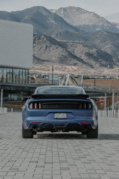 Rear view of a blue sports car against mountain backdrop, emphasizing luxury and power.