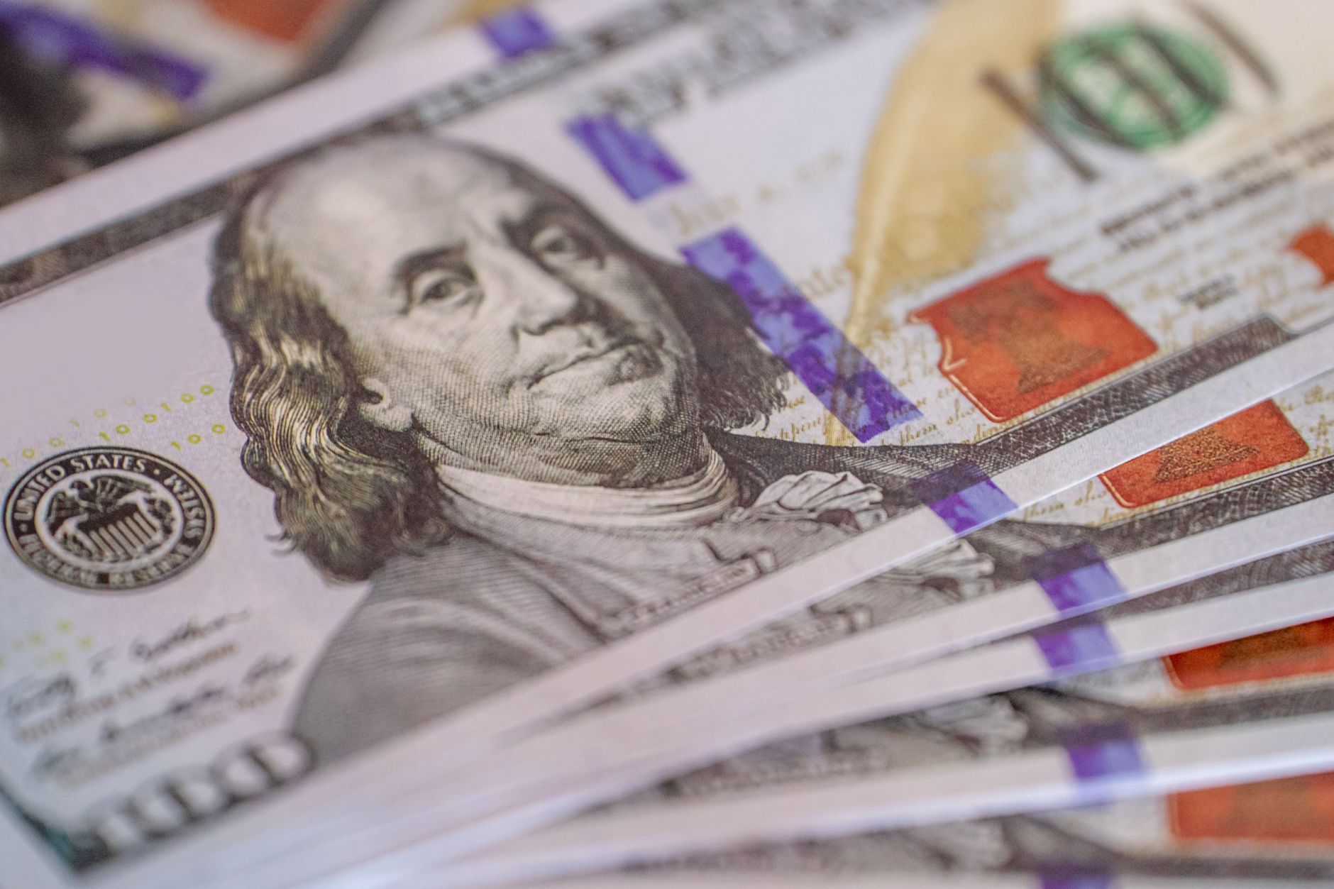 Detailed close-up image of US hundred dollar bills fanned out, showcasing currency detail.