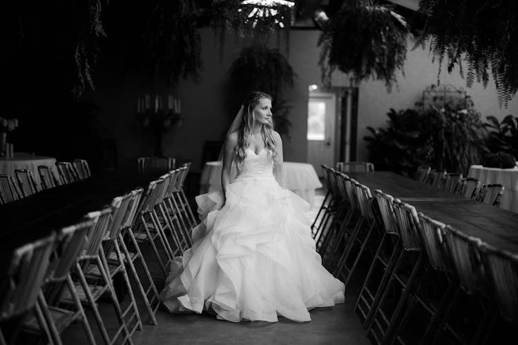 Black And White Photograph Of Bride In Wedding Dress Walking Down Row Of Empty Chairs