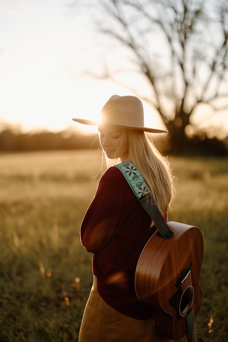 Woman In Field Carrying Acoustic Guitar On Her Back