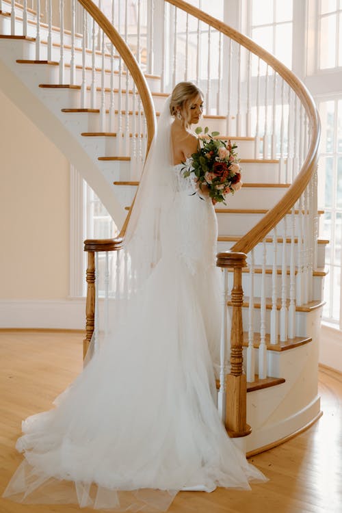 Bride Standing at Bottom of Spiral Staircase Holding Bouquet of Flowers