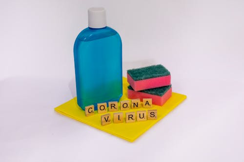A Cleaning Solution on Blue Plastic Bottle Beside Sponges and Scrabble Tiles