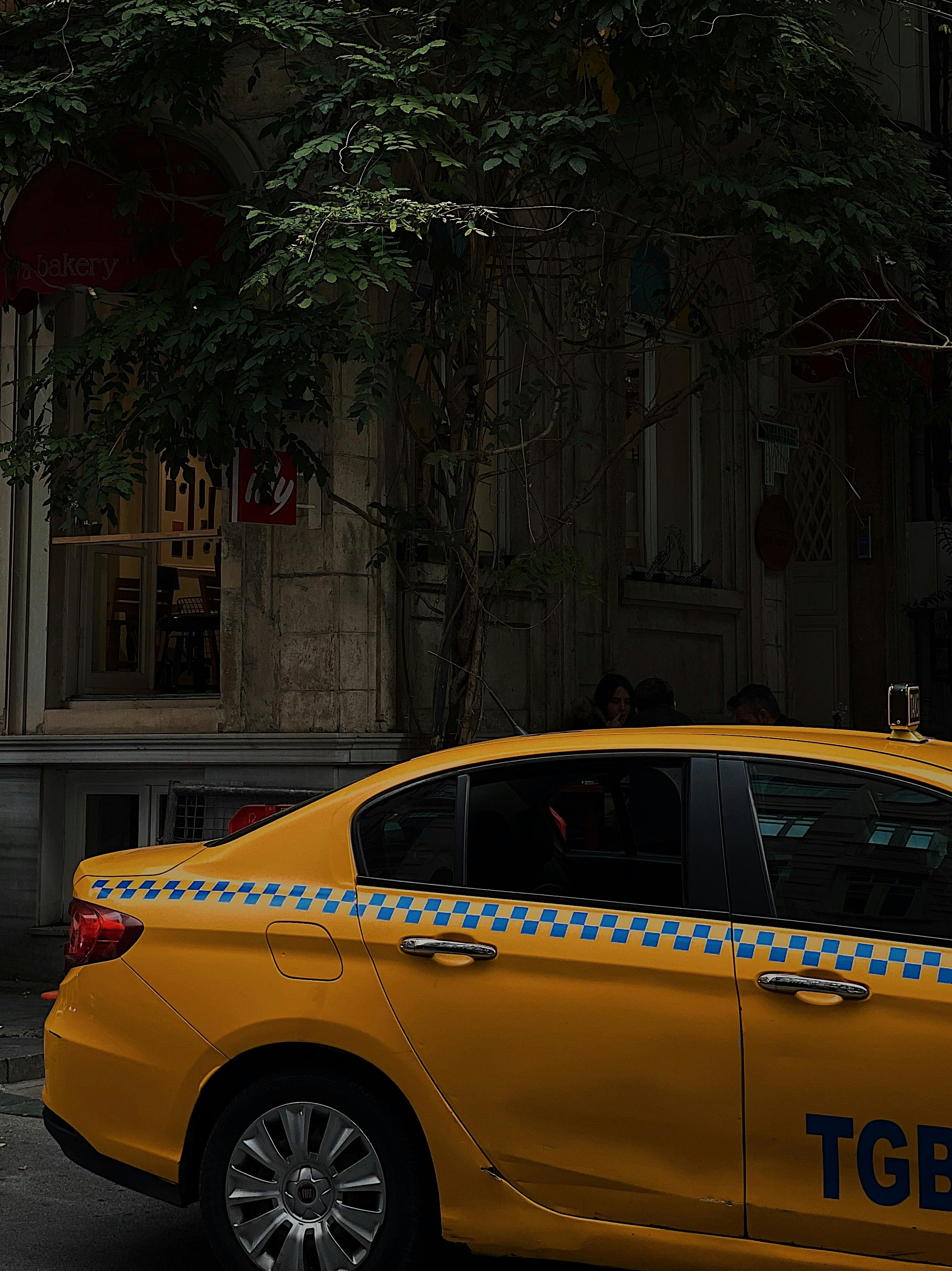 Yellow taxi car parked on a street in Istanbul with trees and buildings in the background.