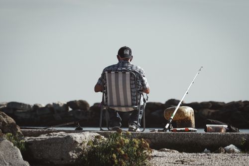 Free Back view of a man fishing by a waterfront, enjoying peaceful leisure time outdoors. Stock Photo