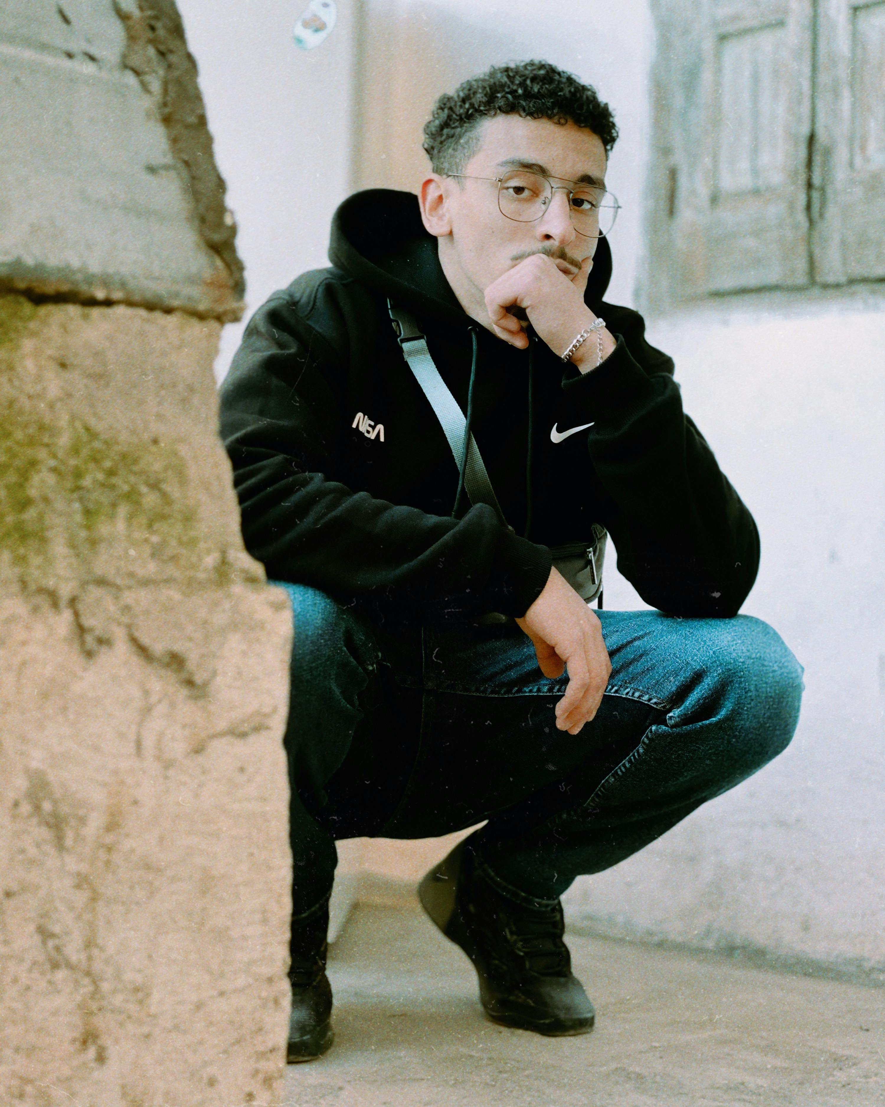 Young man in casual streetwear posing thoughtfully in a rustic alley in Fes, Morocco.