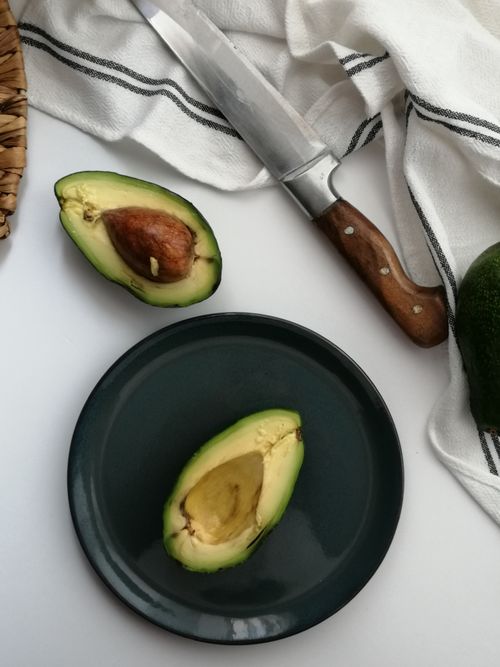 Free Sliced avocado halves with kitchen knife on dark plate, perfect for food photography and healthy eating themes. Stock Photo