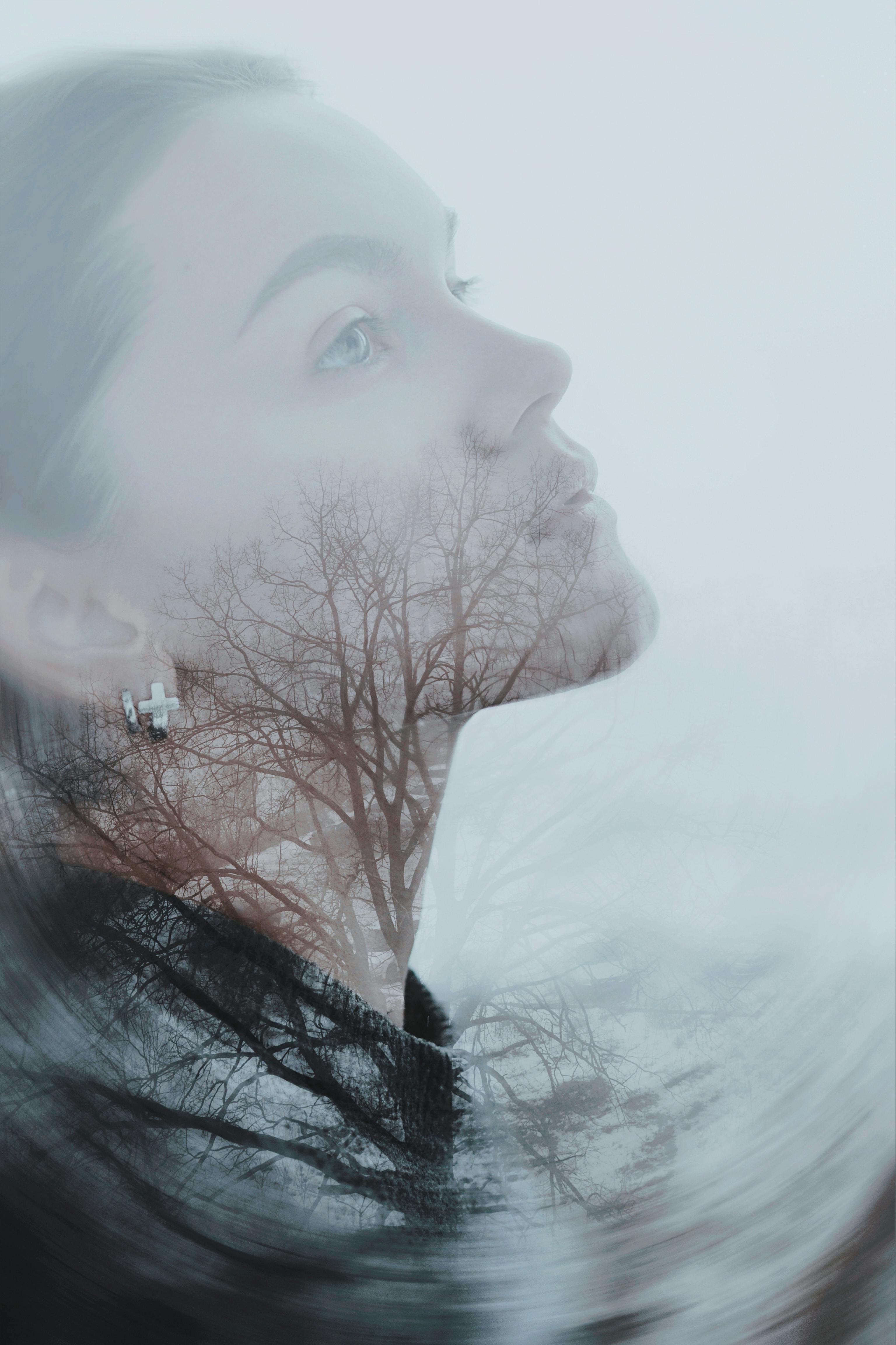 A serene double exposure of a woman's side profile with bare trees, conveying introspection.