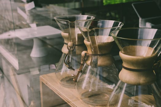 Close-up of Chemex coffee makers on a wooden shelf in a modern cafe setting.