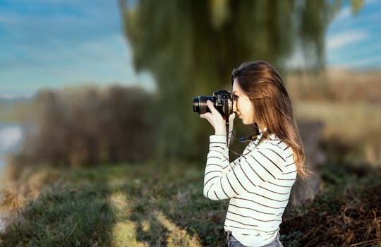 Side view of a young woman photographer in striped outfit using a camera outdoors.