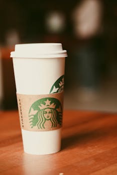 Disposable coffee cup on table in cozy setting, perfect for representing on-the-go lifestyle.