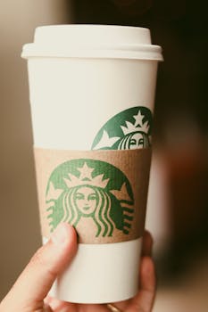 A close-up shot of a hand holding a white coffee cup with a green logo and sleeve.