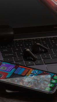 Close-up of a smartphone and wireless earbuds on a laptop keyboard, perfect for tech and lifestyle themes.