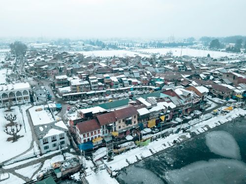 Free Aerial drone footage of a snowy neighborhood in Srinagar, showcasing vibrant rooftops and a frozen landscape. Stock Photo