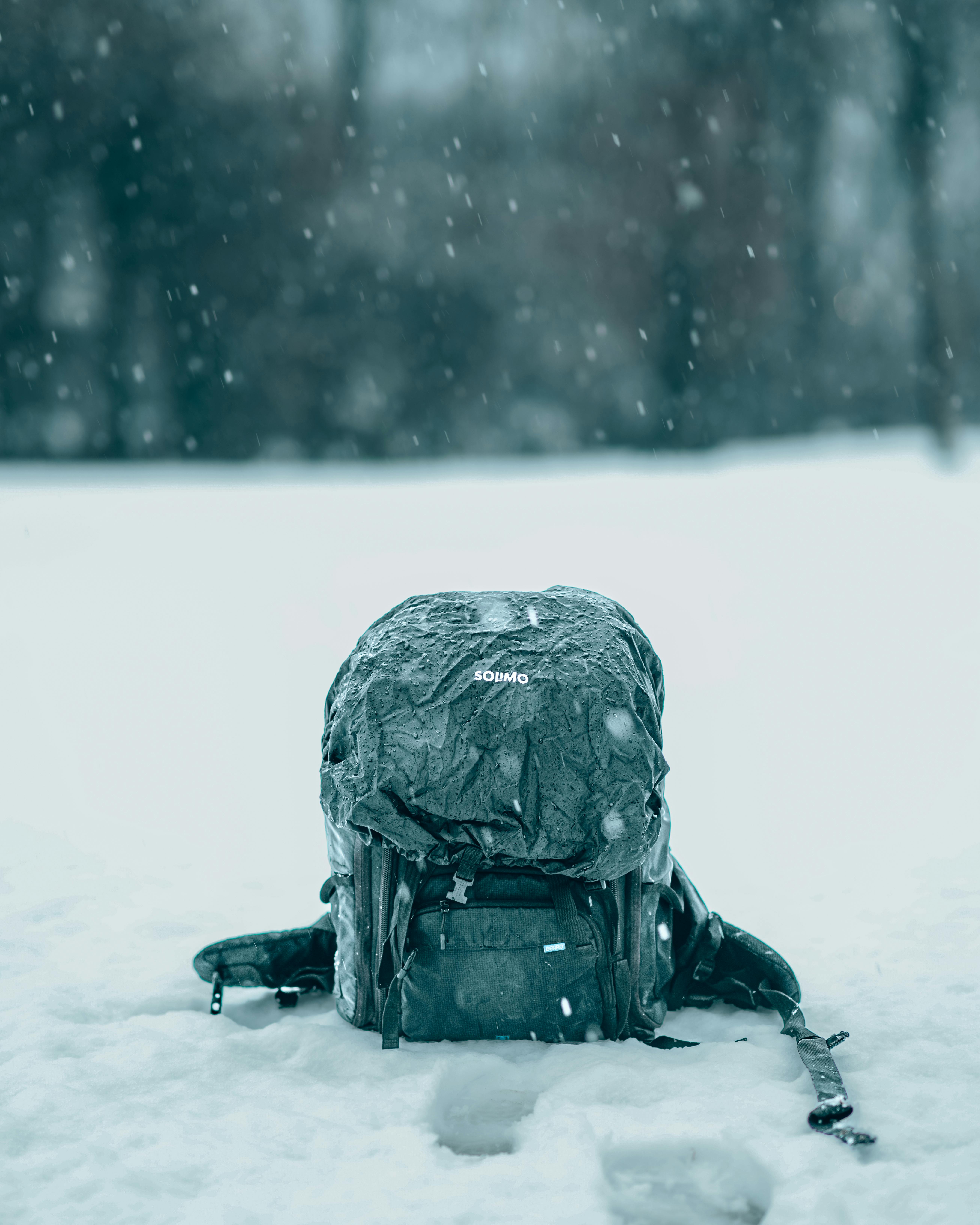 A lone backpack sitting on snowy ground amidst snowfall, capturing the essence of winter adventure.