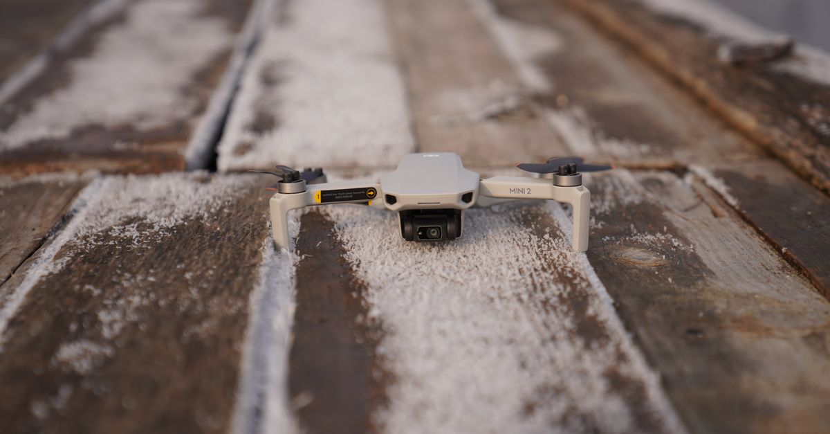 A close-up view of a mini drone resting on a dusty wooden surface, ready for takeoff.