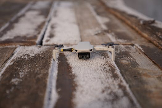 A close-up view of a mini drone resting on a dusty wooden surface, ready for takeoff.