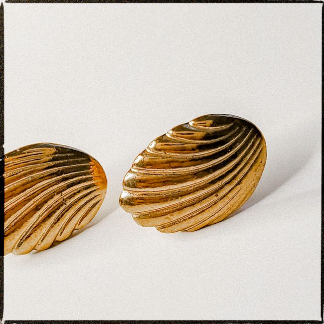 Close-up of elegant gold seashell-shaped earrings on a plain background.