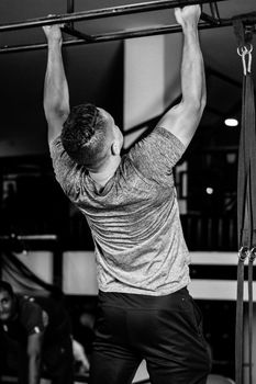 Black and white image of a man performing pull-ups in a gym setting, showcasing strength and fitness.