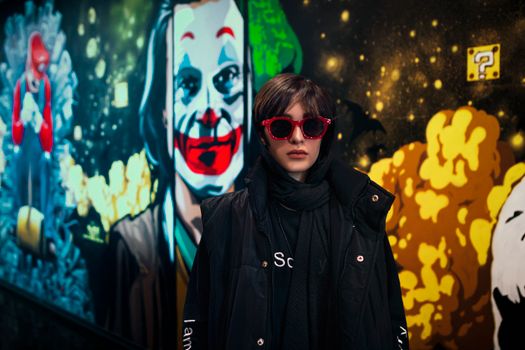 Portrait of a woman in sunglasses posing by a colorful mural in Tehran.