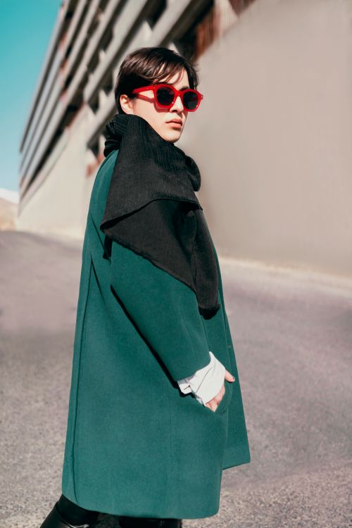 Free Stylish woman in green coat and sunglasses strolling outside on a sunny day. Stock Photo