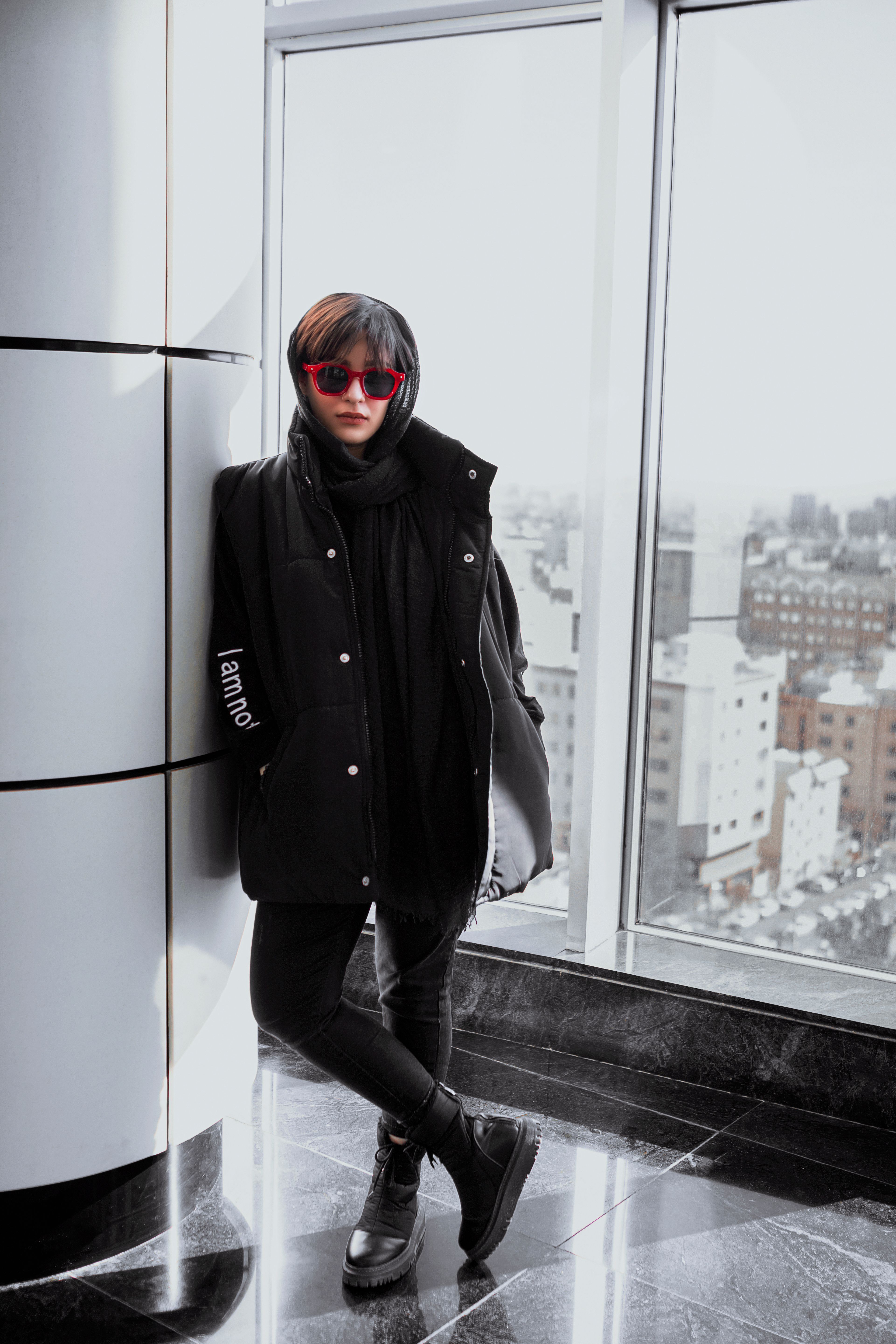 Stylish woman in black clothing stands confidently in a modern building, showcasing urban fashion.