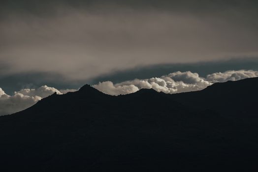 Dark mountain silhouette under dramatic twilight sky with billowing clouds.