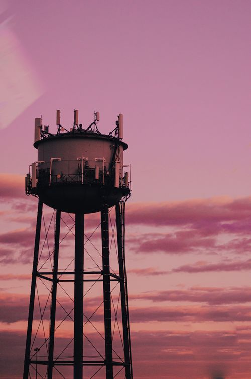 Free Vertical steel water tower silhouetted against a pink sunset sky. Industrial elegance. Stock Photo