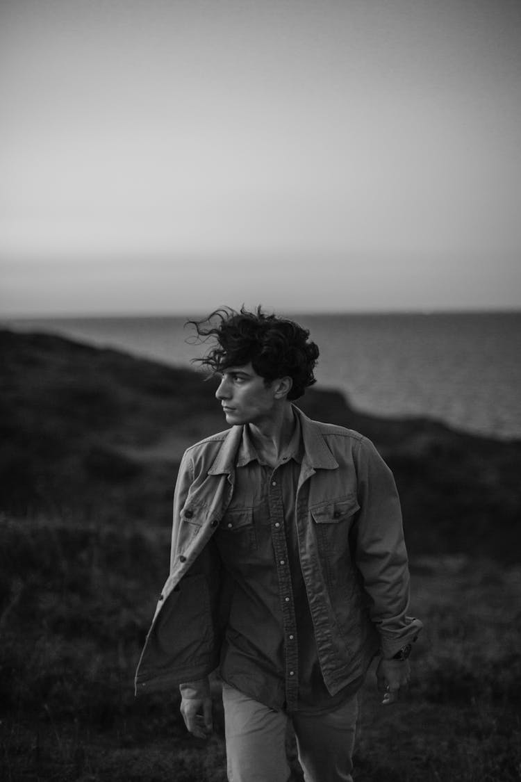 Young Man With Windblown Hair Walking In Meadow At Seaside 