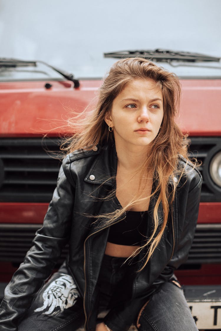 Attractive Young Woman Wearing Black Leather Jacket And Gray Jeans And Red Car In Background