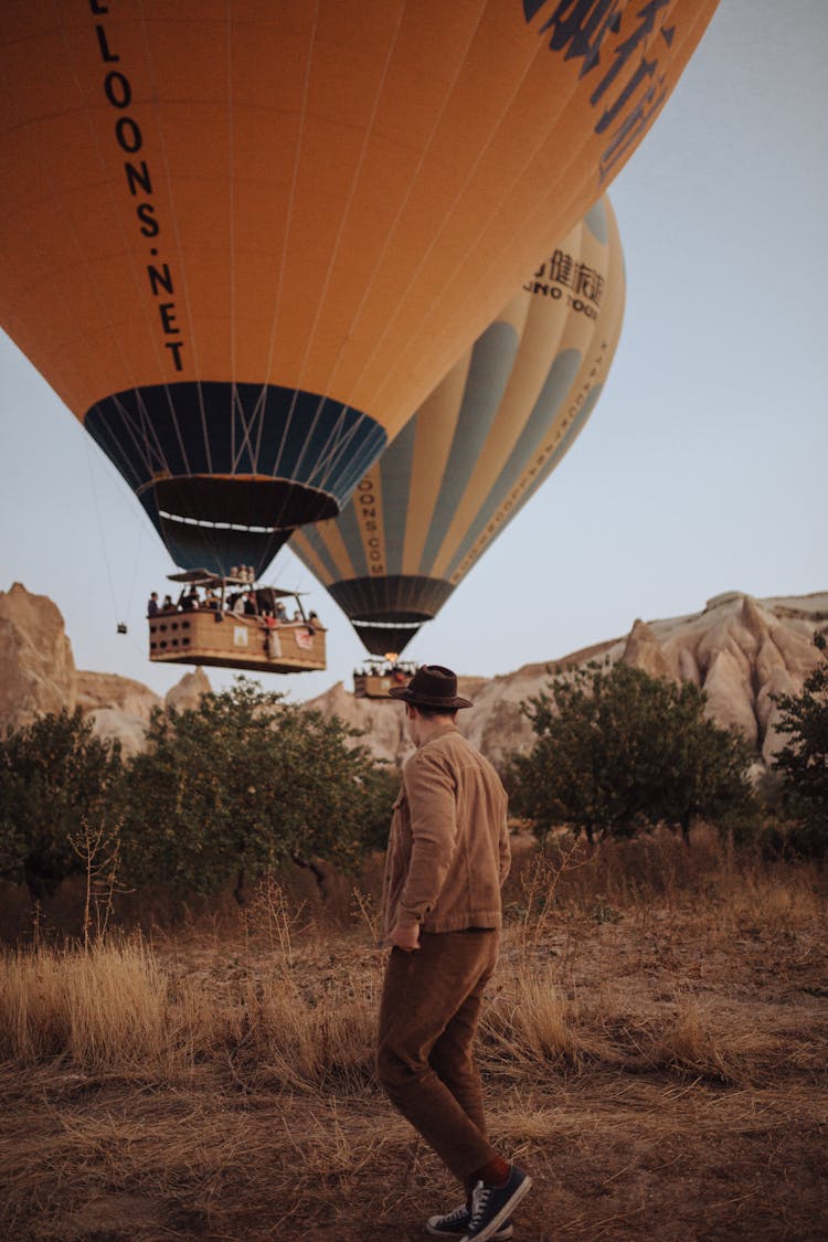 Man In Hat Approaching Balloons Landing On Prairie 