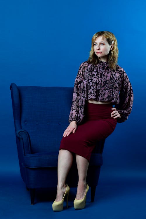 A Woman Posing while Sitting on a Blue Armchair