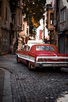 Classic red Chevrolet Impala driving through a narrow cobblestone street lined with historic buildings.