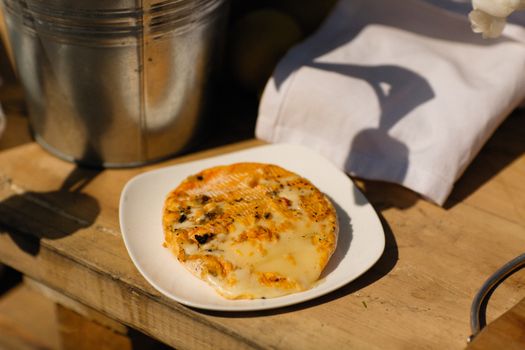 Melted savory cheese on a white plate outdoors in rustic setting.