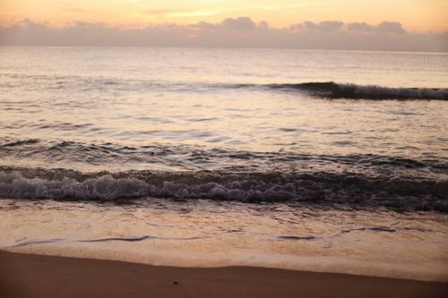 Free A tranquil beach scene featuring gentle waves under a stunning sunset sky. Stock Photo