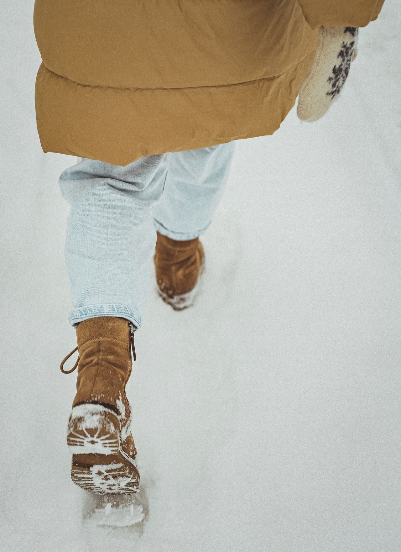 walking through snow in a tan puffer coat and brown boots