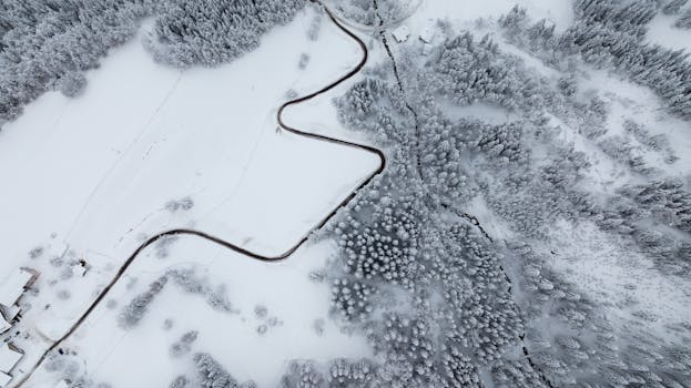 Drone shot of a snow-covered landscape with winding roads and coniferous trees in Villach, Austria.