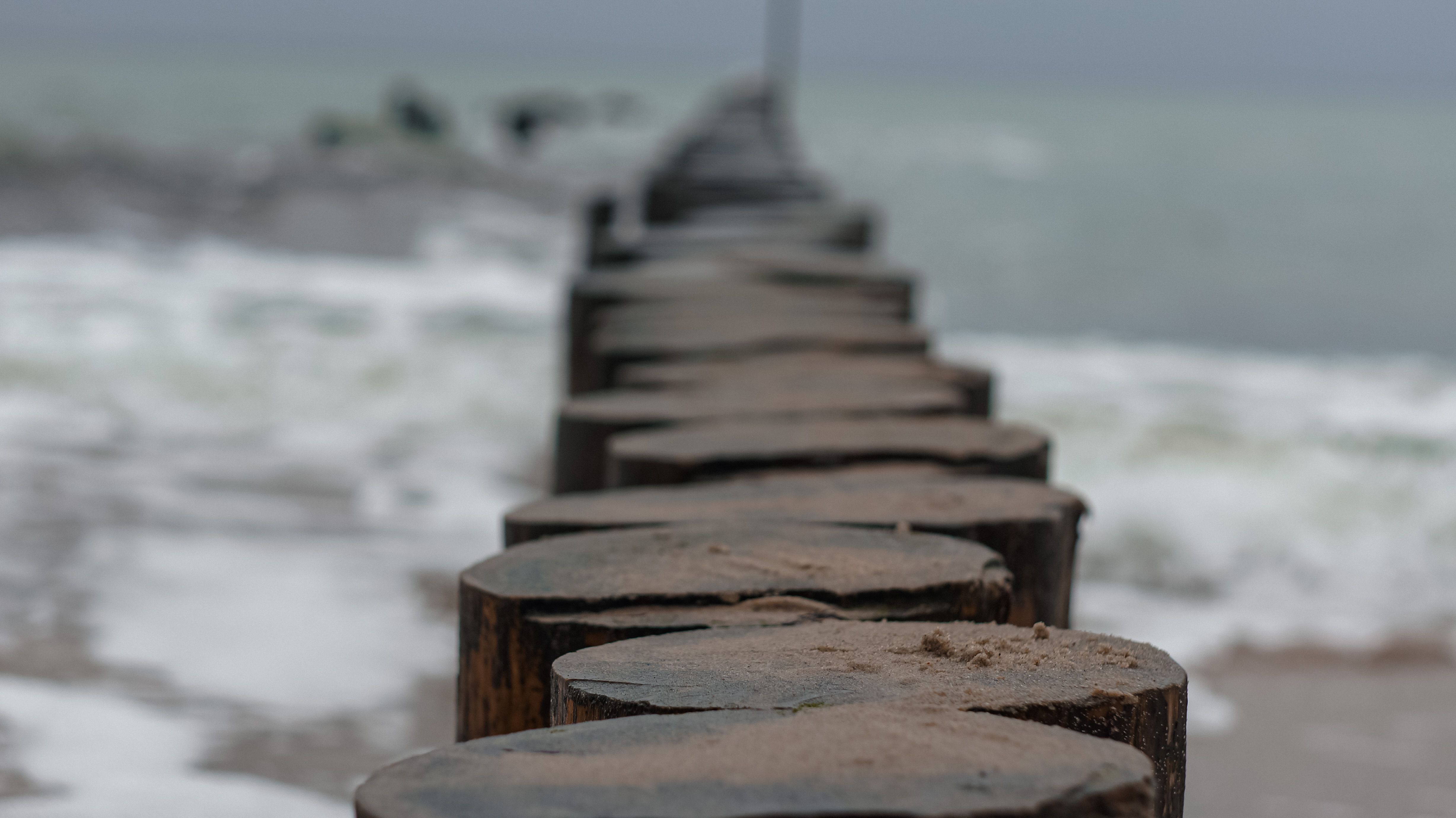 A close-up view of a wooden pier extending into the ocean with waves crashing against the shore.