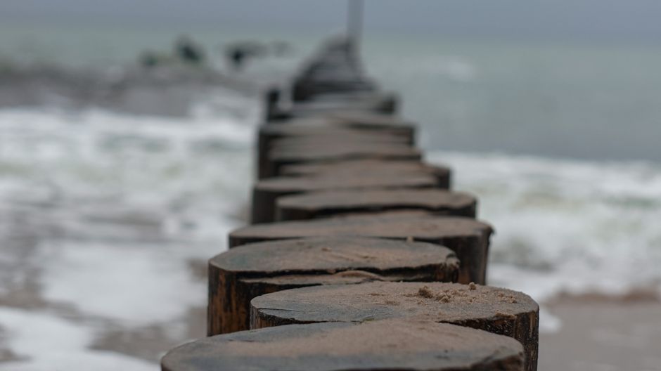 A close-up view of a wooden pier extending into the ocean with waves crashing against the shore.