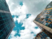 在多云的蓝天下，低角度的城市景观中矗立着摩天大楼，一架飞机正飞过