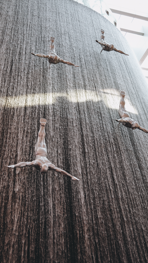 Free Artistic sculptures of divers in a stunning vertical waterfall display at Dubai Mall. Stock Photo
