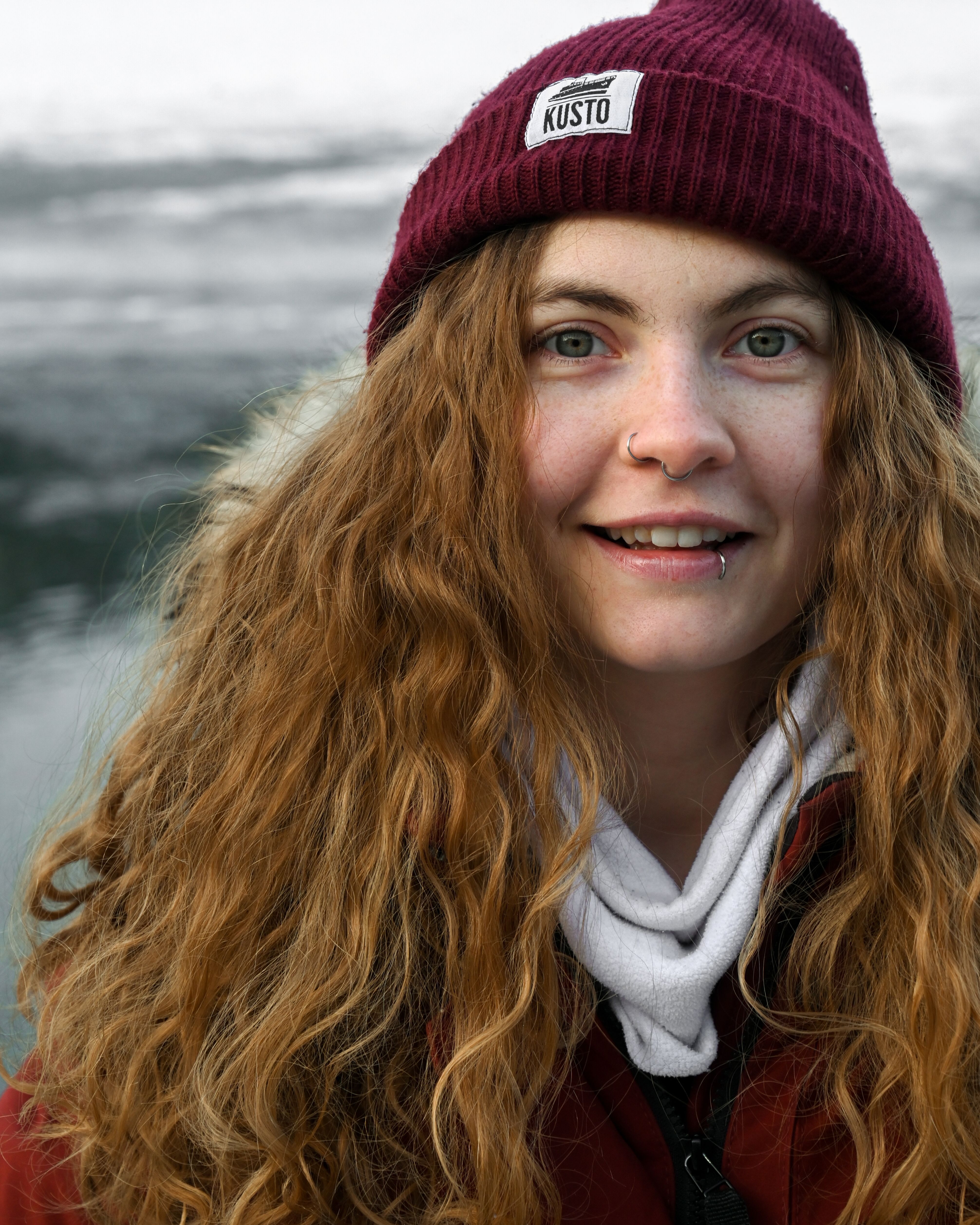 Portrait of a happy woman with curly hair and nose piercing, wearing a beanie in winter.