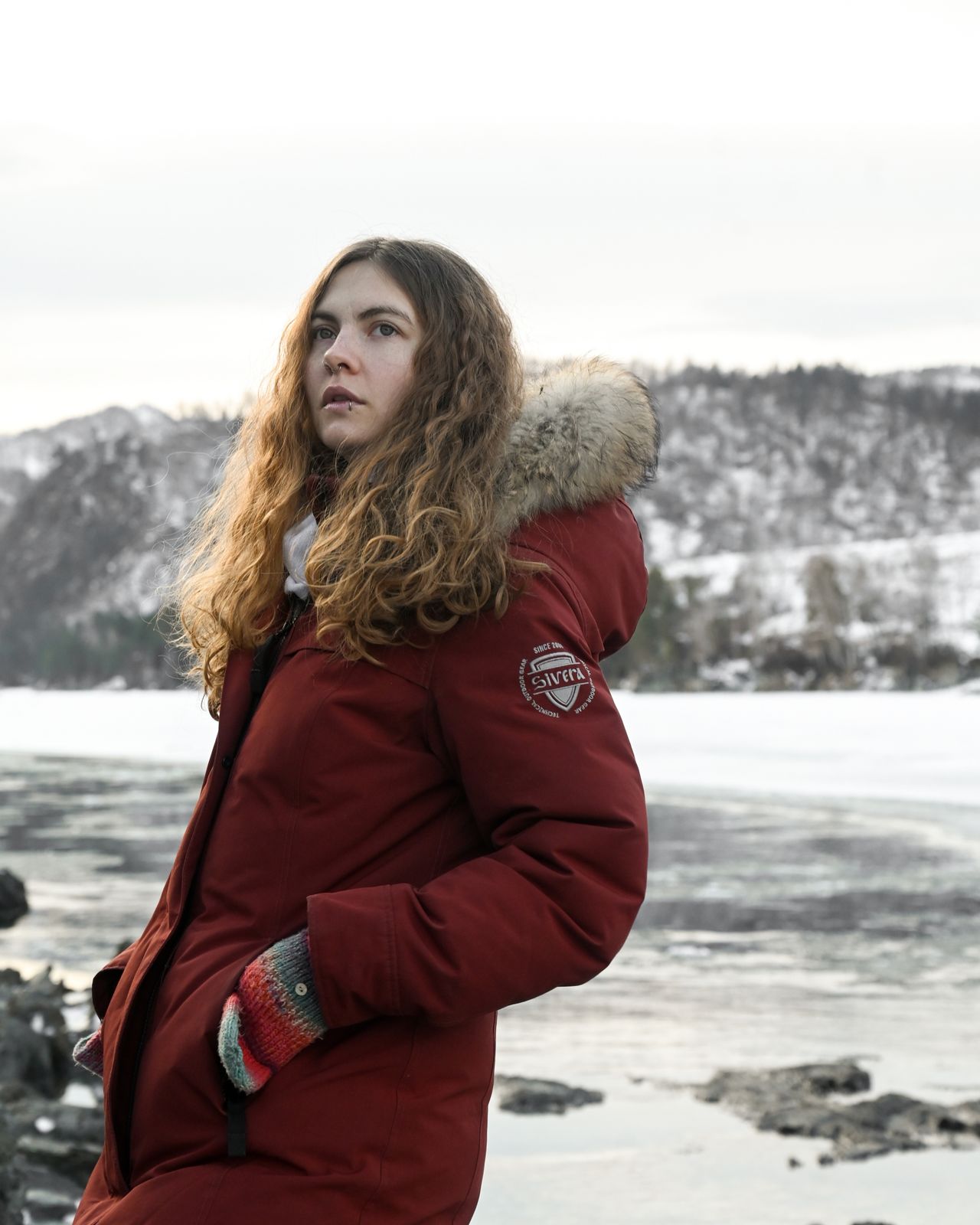 Woman in a red parka standing by a frozen lake