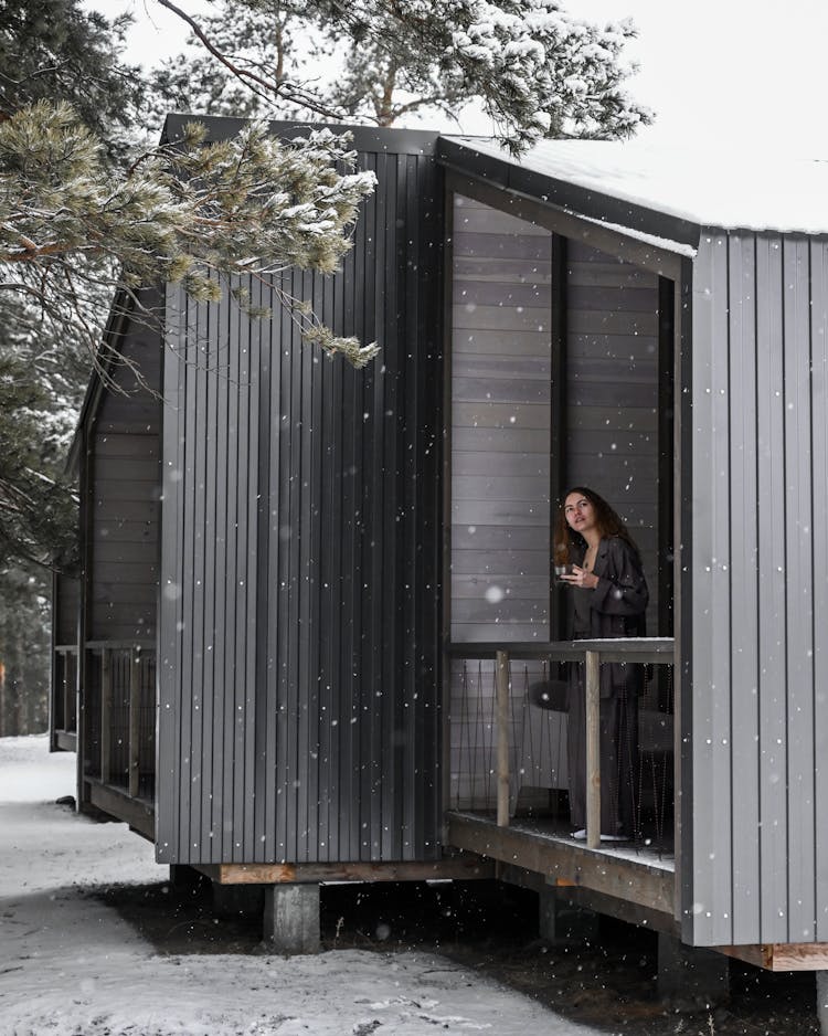 Woman Standing On Balcony Watching Falling Snow