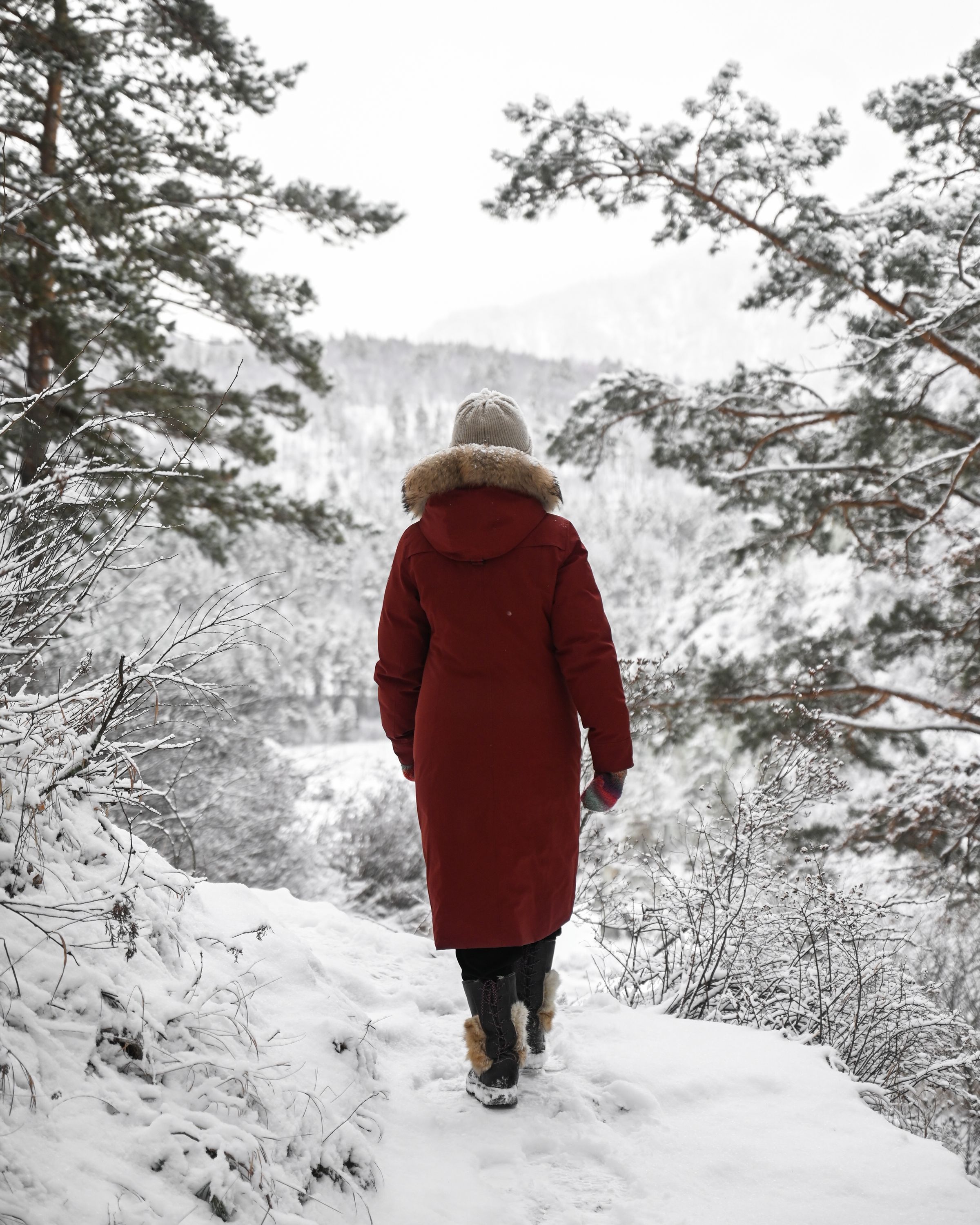 Woman in a red winter coat walking through a snowy landscape