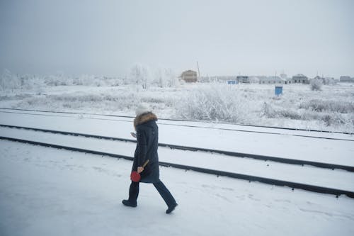 One Caucasian female in winter clothes standing near rails