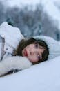 Woman in White Winter Coat Lying on Snow Covered Ground