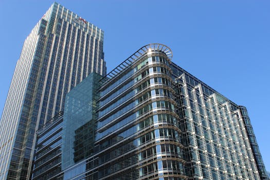 A modern office building with glass panels in Canary Wharf's business district under a clear blue sky.