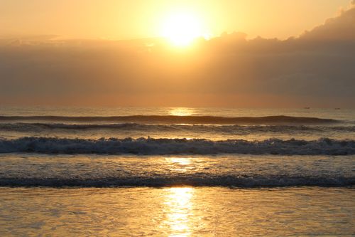 Free Golden sunset over the ocean with gentle waves creating a tranquil scene. Stock Photo