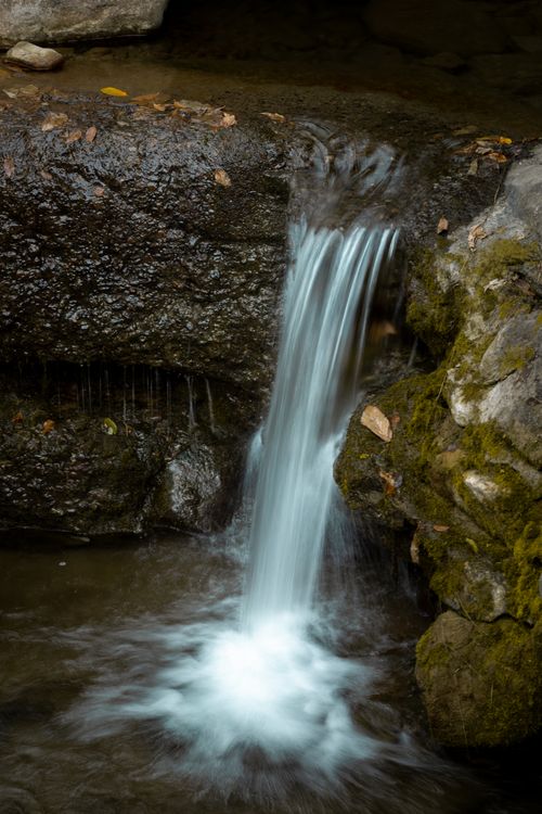 Free A tranquil small waterfall flowing over moss-covered rocks, captured in a natural setting. Stock Photo